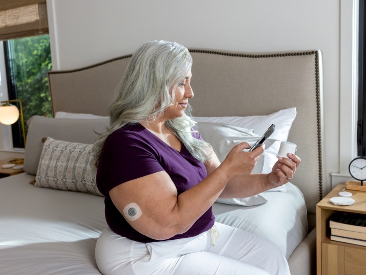 Some sitting upright on the edge of a bed using the Dexcom Stelo app on their phone