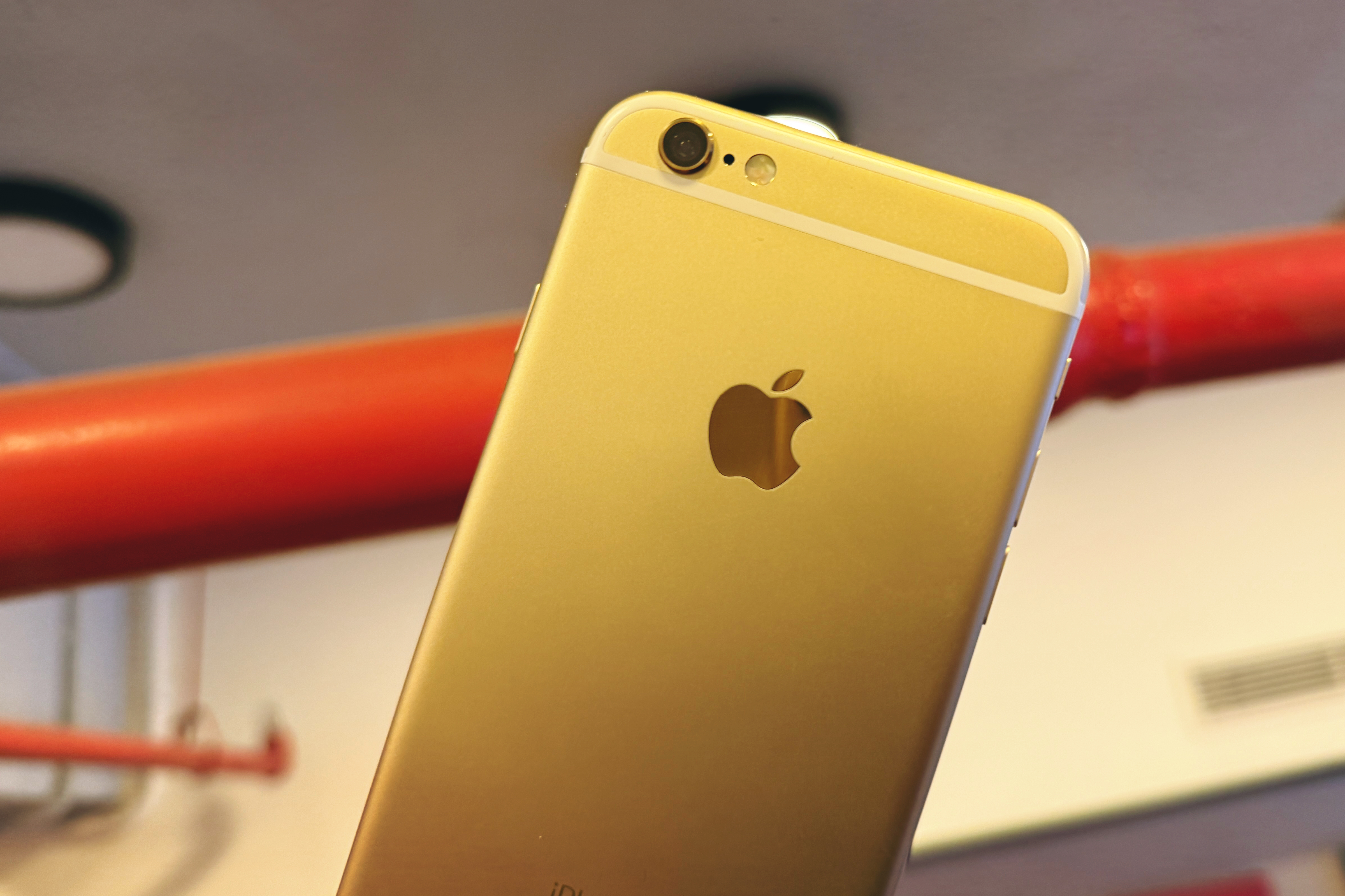 Alt text: An iPhone 6S in gold held against a red pipe, highlighting its slim design.