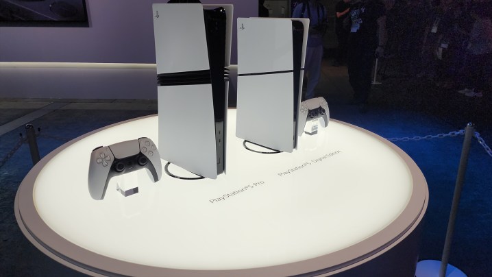 A lit table holds a PS5 Pro, and a PS5 all digital, the former standing noticeably taller.