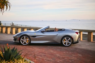 Alt text: A red Ferrari Portofino convertible being driven on a scenic coastal road.