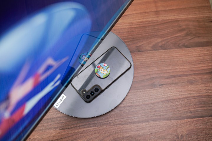 A phone charging wirelessly on the base of the Lenovo Yoga AIO 9i, demonstrating the convenient charging feature.