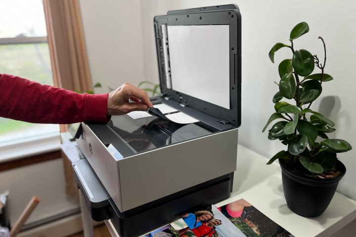 A person places photos on the HP OfficeJet Pro 9015e’s flatbed scanner glass.