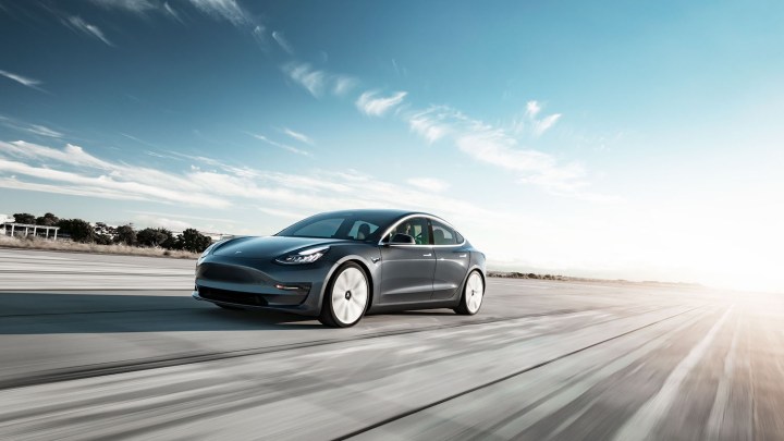 A Telsa Model 3 drives along a road.