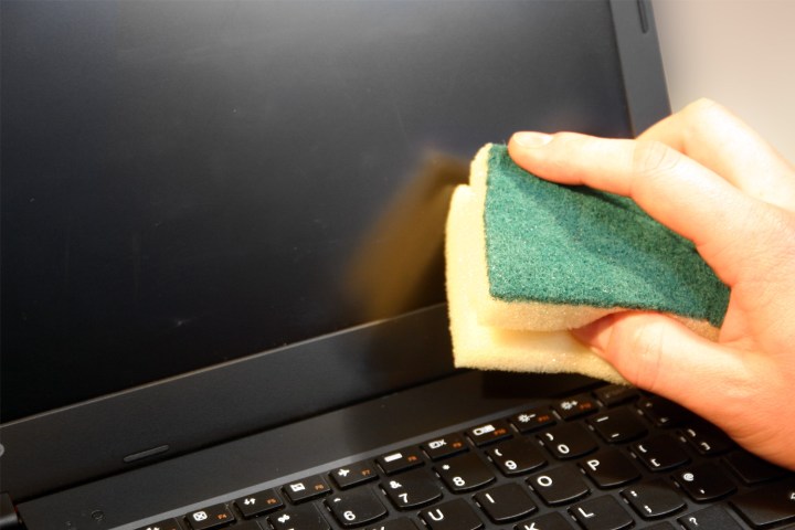 A person cleaning a laptop screen with a damp sponge.