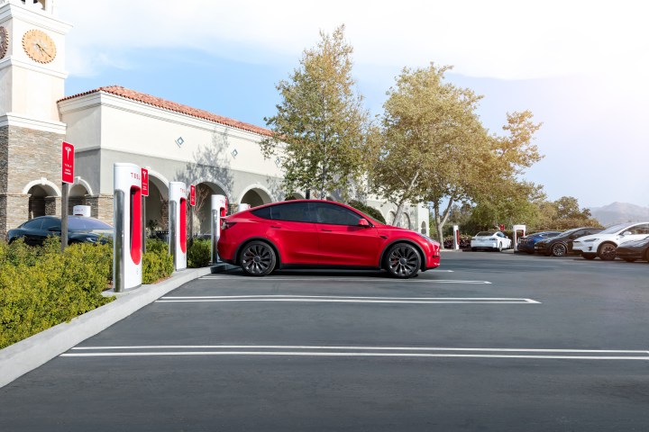 alt text: A red Tesla car charging at a Tesla Supercharger station.