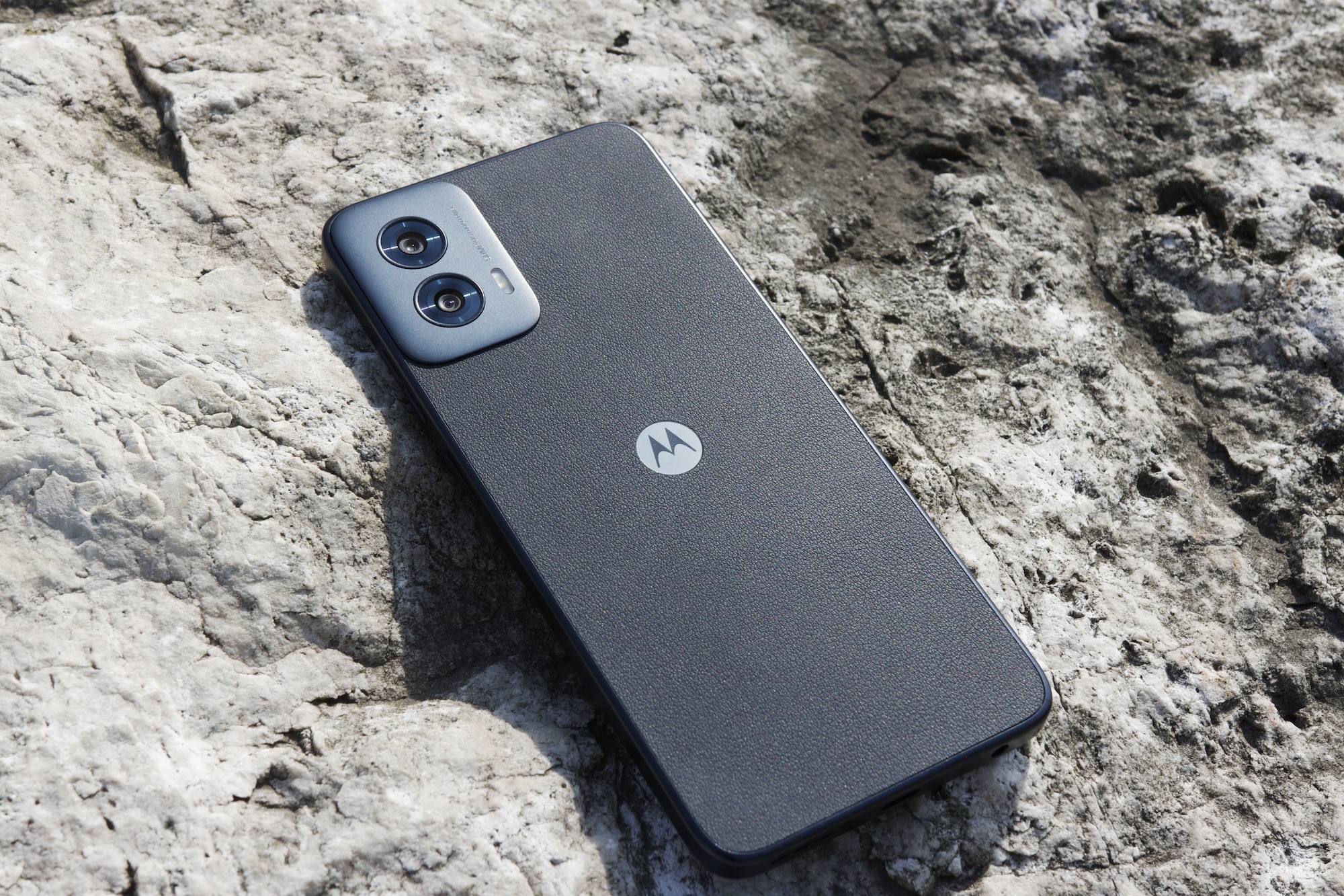 Alt: The Moto G Power 5G (2024) smartphone resting on a rock outdoors.