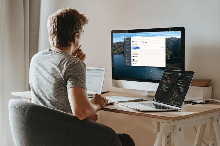 A person using 1Password on a desktop all-in-one computer while sat at a desk. There are two laptops next to them on the desk.