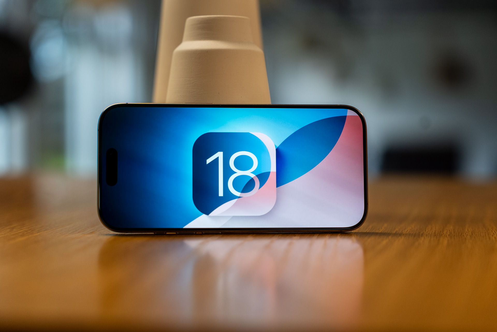 alt: The iOS 18 logo displayed on an iPhone 16 Pro.