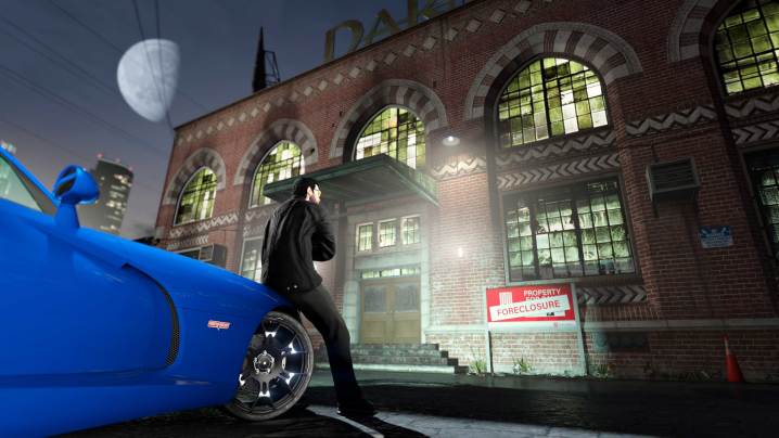 A guy leaning on a blue car in front of a big brick foreclosed building in GTA Online.