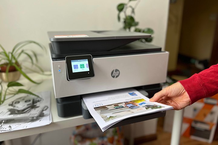 A person retrieves a stack of documents from the HP OfficeJet Pro 9015e’s paper tray.