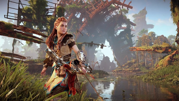 Aloy standing in knee-deep water with her bow and arrow in front of some ruins.