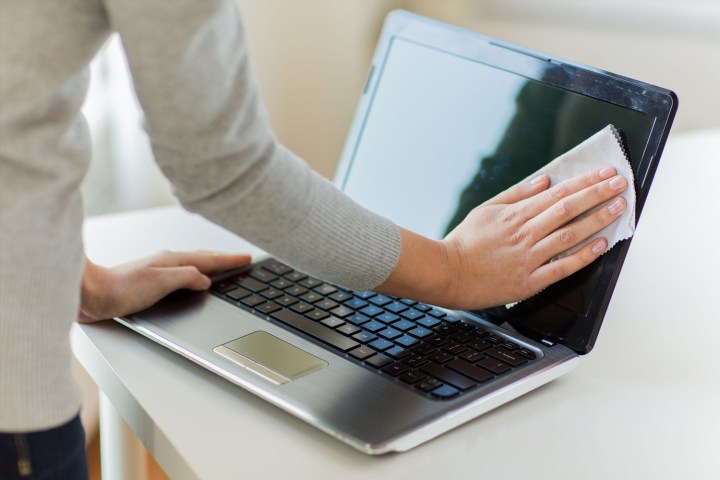 A person cleaning a laptop screen with a microfiber cloth.