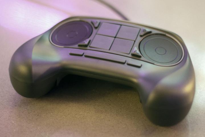 A Steam Controller from Valve on a surface. You can see two track pads on top with four buttons in the middle.