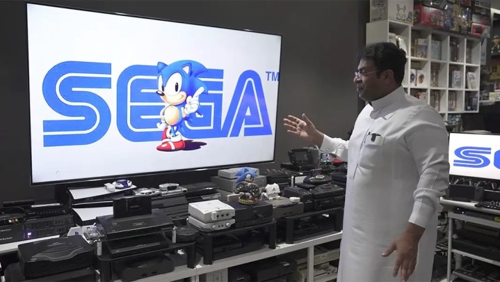 A room filled with various video game consoles, with the Sega logo displayed prominently on the TV screen.