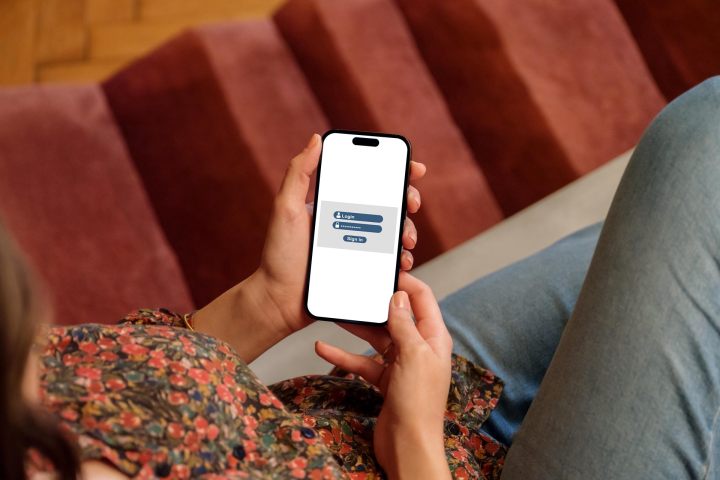 alt=A woman holding an iPhone displaying a login screen.