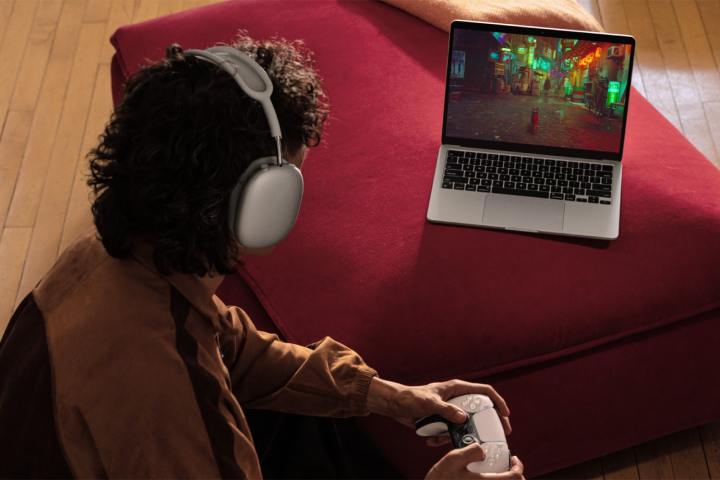 alt text: A person playing a video game using a PlayStation controller on a MacBook Air.