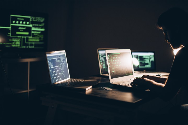 An individual surrounded by several computers typing on a laptop.