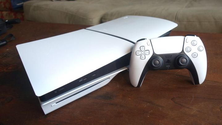 A PS5 sits on a table with a DualSense standing up next to it.