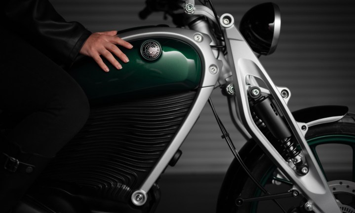 Alt: Close-up view of the Royal Enfield Flying Flea FFC6 electric motorcycle's tank area and front fork, showcasing its design and components. A rider is visible in the seat.