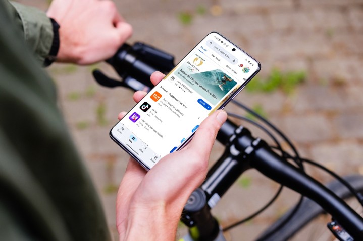 A person holding an Android phone while on a bike. The display shows the Google Play Store.