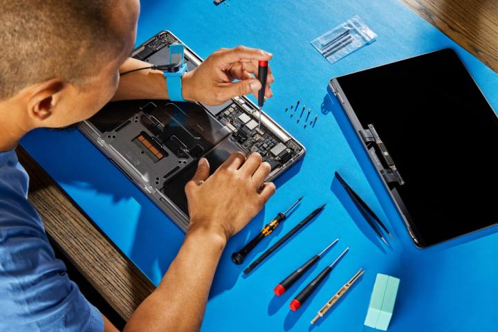 A person repairing a MacBook on a blue table.