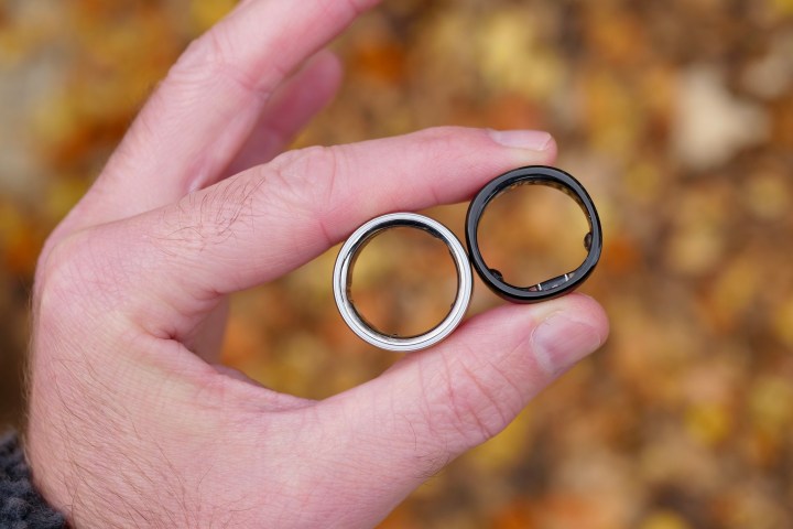 Alt: A close-up view of the Oura Ring 4 and RingConn Gen 2 held between fingers, highlighting their different designs and finishes.