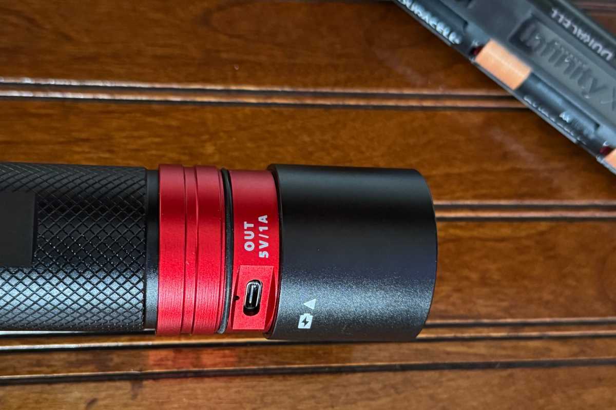Detail of the Infinity X1 flashlight's base with its protective cap twisted open, revealing the USB-C input port for battery charging and USB-C output port for powering other devices.