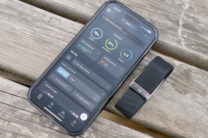 The Whoop 5.0 fitness tracker module placed next to a smartphone displaying the Whoop app interface.