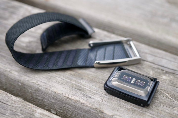 The Whoop 5.0 fitness tracker module detached from its fabric strap, lying on a surface.