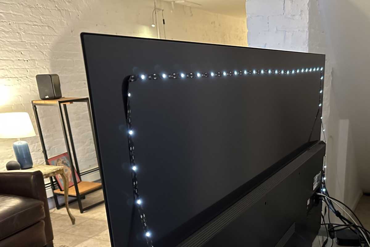 Close-up of a white LED bias light strip being installed on the back panel of a television set for improved picture quality.