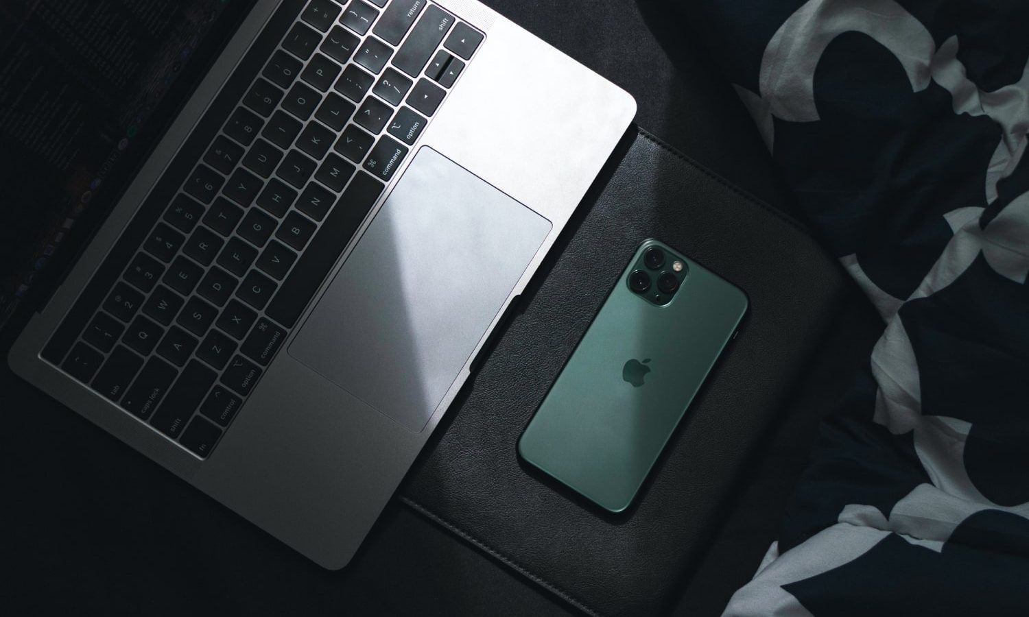 alt: A dimly lit photo of a MacBook and iPhone resting on a surface.