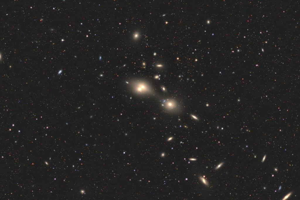 Wide-field astronomical image capturing two distant merging galaxies, where a quasar's energetic beam from one galaxy impacts the other, an event dubbed a 'cosmic joust' observed in the early universe.
