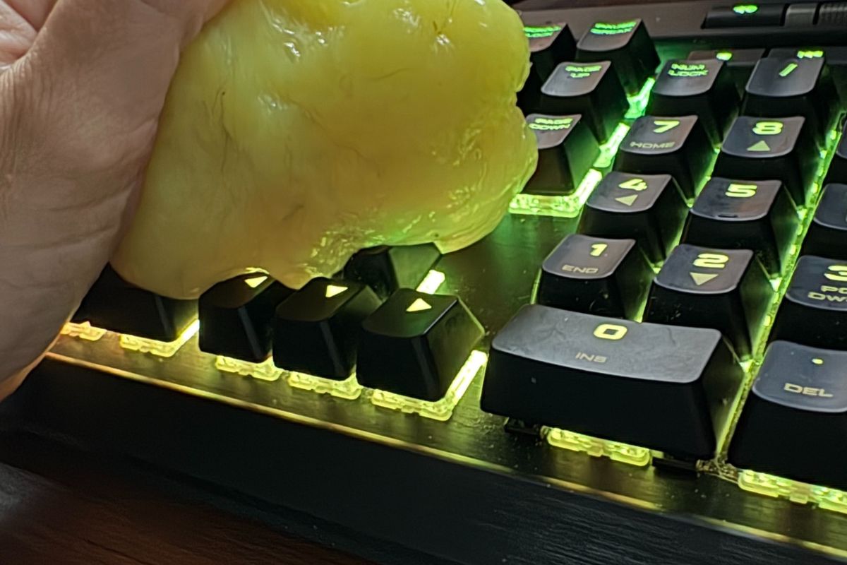 Yellow cleaning slime being pressed onto a dirty keyboard to remove dust and crumbs.