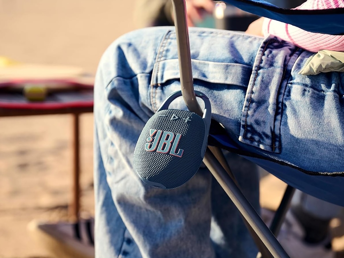 JBL Clip 5 portable Bluetooth speaker clipped to a beach chair, ideal for outdoor music.